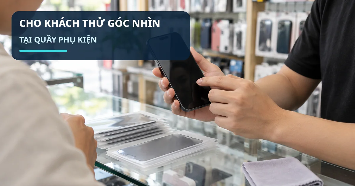Nhân viên quầy phụ kiện cầm điện thoại có màn hình tối ở góc nghiêng để hướng dẫn khách kiểm tra kính chống nhìn trộm.